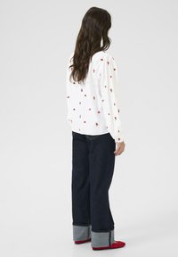 Witte lange mouwen shirt met kleine rode hartpatronen, gecombineerd met donkerblauwe jeans met omgeslagen denim boorden en rode schoenen.