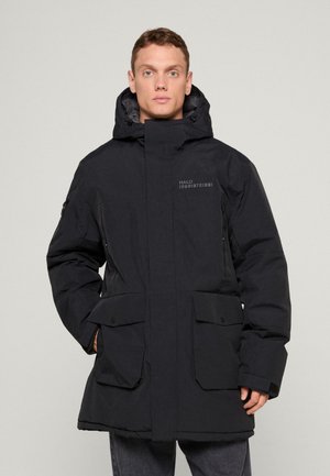 Veste noire rembourrée avec un col montant, poches avant doubles et un logo discret. Fabriquée en matériau texturé et imperméable.
