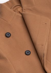 Manteau en laine marron chameau avec des boutons noirs et des boutonnières visibles, montrant une partie du revers et du col.