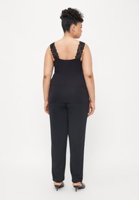 Schwarzes ärmelloses Top mit Spitze-Trägern, kombiniert mit schwarzen Hosen. Glatter Stoff mit einer figurbetonten Silhouette, die ein schlichtes, elegantes Design zur Schau stellt.