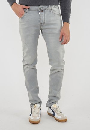 Lichtgrijze denim jeans met een slim fit, vijf-pocketontwerp en subtiele stikdetails. Gecombineerd met witte en marineblauwe sneakers.