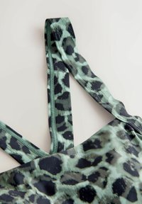 Sportoberteil mit Leopardenmuster in grün-schwarzer Farbgebung, mit verstellbaren Trägern und glattem, dehnbarem Stoff.