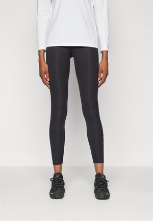 Leggings deportivos negros con un diseño ajustado, textura suave, cintura de altura media y detalle del logo a lo largo del lado izquierdo; combinados con zapatillas negras.
