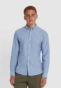 Camicia azzurra chiara in tessuto chambray, con colletto, maniche lunghe e un piccolo logo ricamato sul petto.