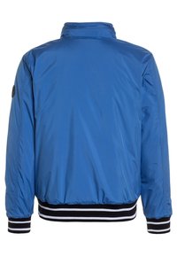 Giacca bomber in nylon blu con texture liscia, polsini e orlo a costine neri e bianchi, e colletto alto. Senza chiusure o tasche visibili.