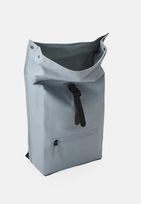 Sac à dos étanche gris à rouleau avec une boucle noire, comporte une poche avant zippée et une texture lisse et durable.