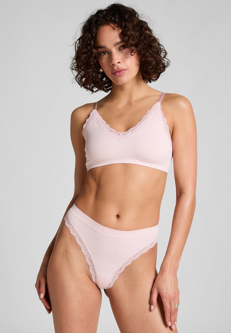 Lichtroze geribbelde bralette en bijpassende hoge thong. Fijne kantafwerking langs de randen. Zachte textuur, verstelbare bandjes op de bralette.