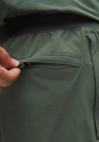 Mano che tiene la cerniera di una piccola tasca con zip su pantaloni o pantaloni corti sportivi di tessuto verde.