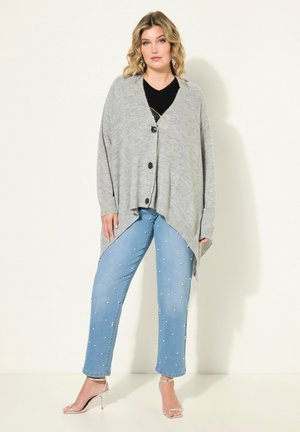 Grauer Strickcardigan mit V-Ausschnitt und schwarzen Knöpfen, kombiniert mit hellblauen Jeans mit Perlenverzierungen und klaren Riemchensandalen.