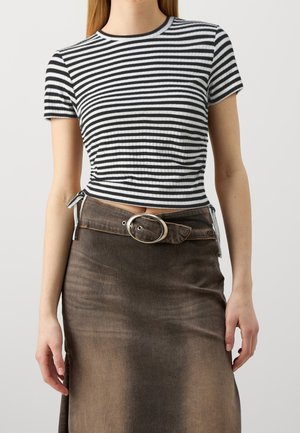 Woman wearing a black and white striped fitted crop top paired with a brown high-waisted skirt featuring a large oval belt buckle.