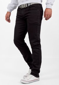 Zwarte denim jeans met een slim fit, voorzien van vijf zakken en knoopsluiting. Gecombineerd met witte sneakers en een grijze riem.
