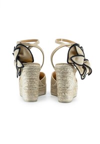 Sandali platform in espadrillas beige con tacchi in juta intrecciata, cinturini alla caviglia regolabili e un accento decorativo di un fiore in tessuto contornato di nero.
