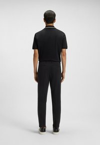 Czarna koszulka polo z krótkim rękawem i minimalnym kołnierzykiem, połączona z czarnymi spodniami i ciemnymi butami, widok od tyłu.