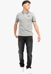 Grå polo-shirt med krave, tre knapper og blå stribede detaljer. Kombineret med mørke jeans og hvide sneakers. Enkel design.