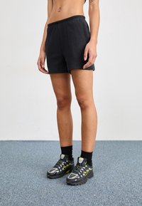 Black ribbed athletic shorts with an elastic waistband, paired with black and grey shoes featuring yellow accents and black socks.