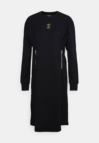 Svart klänning i mjukt tyg, med långa ärmar, avslappnad passform och två frontfickor med dragkedja. Guldbladssymbol på bröstet.