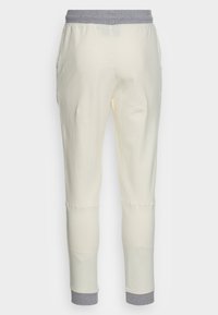 Krämfärgade joggerbyxor med ett grått elastiskt midjeband, smalnande ben och sidofickor. Mjuk bomullsmaterial, slät textur.