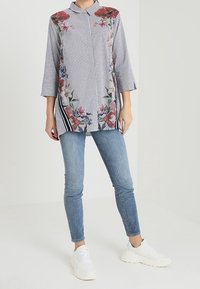 Tuniki w paski z kwiatowym haftem w czerwieni i odcieniach niebieskiego, z kołnierzykiem, rękawami do połowy przedramienia i bocznymi rozcięciami. Noszona z dżinsami i trampkami.