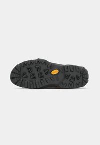 Sola de bota de caminhada preta com sulcos profundos, padrões multidirecionais e um logotipo amarelo da Vibram no centro, sobre um fundo branco.