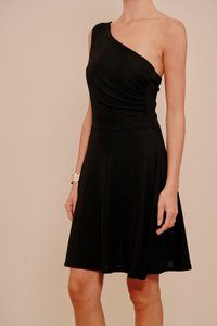 Crna haljina na jedno rame izrađena od mekog, teksturiranog tkanja s pripijenim strukom i suknjom koja se širi. Ima suptilni sjaj i naborane dizajnerske detalje.