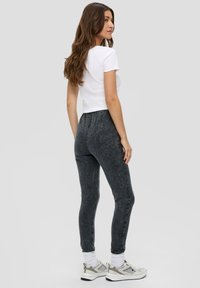 Szare legginsy z efektem przetkania, wykonane z elastycznego materiału, zestawione z białą dopasowaną koszulką i jasnymi trampkami z srebrnymi akcentami.