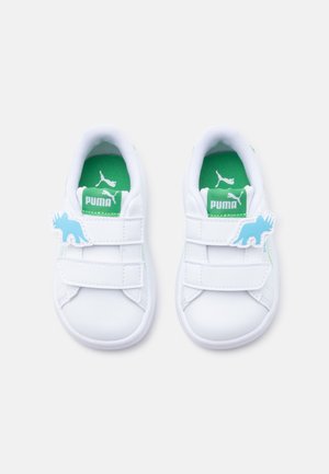 Chaussures blanches Puma pour tout-petits avec semelles intérieures vertes, deux brides Velcro et décorations bleues en forme de dinosaure sur les brides extérieures.