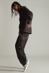 Chaqueta negra con cierre de botones, pantalones cargo negros y zapatos slip-on blancos a cuadros. Cadenas sujetas a los pantalones. Diseño simple y moderno.