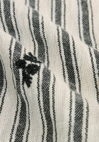 Tissu rayé noir et blanc présentant un tissage texturé, avec de petites broderies florales noires sur un fond plus clair.