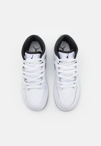 Egy pár fehér magas szárú sportcipő fekete belső béléssel és Jumpman logóval a nyelveken, felülnézetből, fehér háttérrel.