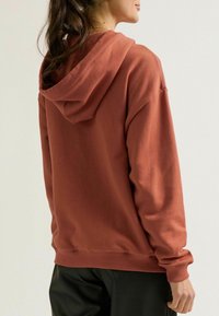 Bordeauxfarbener Hoodie aus weichem Material, mit gerippten Säumen und einer Kängurutasche. Verfügt über eine verstellbare Kapuze mit Kordelzug und ein lässiges Design.