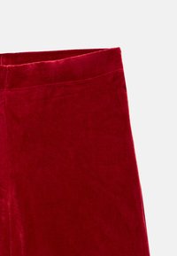 Punaiset samettihousut, joissa on sileä pinta, suora lahjemalli ja siisti vyötärönauha. Ei näkyvissä olevia metalliosia tai kuvioita.