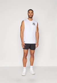 Camiseta blanca sin mangas con logo negro de NY, combinada con pantalones cortos negros y zapatillas blancas. Diseño sencillo, material de algodón, corte atlético.