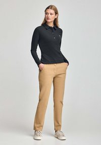 Polo negro de manga larga con tapeta de botones combinado con pantalones beige ajustados y zapatillas ligeras. Tela suave, corte a medida, diseño minimalista.