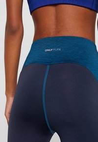 Leggings a vita alta di un blu scuro con un cintura testurizzata color teal con il logo "ONLY PLAY". Tessuto liscio, design aderente e cuciture a contrasto.