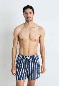 Marineblaue Badeshorts mit weißen vertikalen Streifen, ausgestattet mit einem elastischen Bund und Kordelzug. Glatter Stoff mit leichtem Glanz.