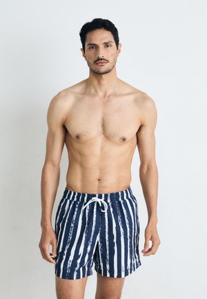 Marineblaue Badeshorts mit weißen vertikalen Streifen, ausgestattet mit einem elastischen Bund und Kordelzug. Glatter Stoff mit leichtem Glanz.