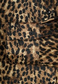 Tela con estampado de leopardo en negro y marrón. Presenta un bolsillo frontal con cierre de botón negro. Textura suave con un acabado brillante.