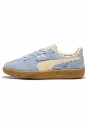 Lichtblauwe suède Puma-sneaker met crèmekleurige streep en rubberen zool, van opzij bekeken tegen een witte achtergrond.