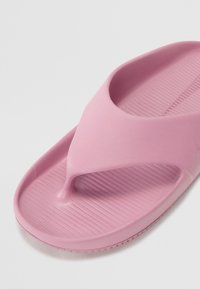 Rosa flip-flop laget av glatt gummi, med en V-formet rem og strukturert såle med horisontale spor for godt grep.
