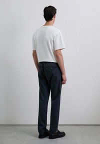 Camiseta de algodón blanca y pantalones oscuros de ajuste relajado. Los pantalones cuentan con una cinturilla elástica y un bolsillo trasero con detalle de botón.
