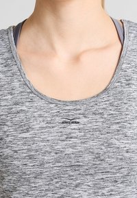Graues Sportoberteil mit einem Rundhalsausschnitt, das aus einem strukturierten Stoff besteht und ein dezentes "VENICE BEACH"-Logo in der Nähe des Kragens aufweist.