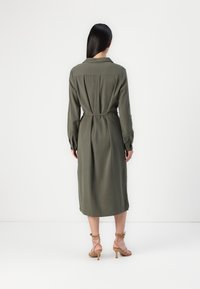 Vestido longo verde-oliva com mangas longas e cinto na cintura, apresentando um colarinho clássico e uma textura suave.