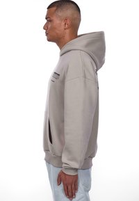 Hellgraues Hoodie mit Kängurutasche, mit gerippten Bündchen und Kapuze mit Kordelzug. Schlichtes Design mit minimalem Branding auf der Vorderseite.