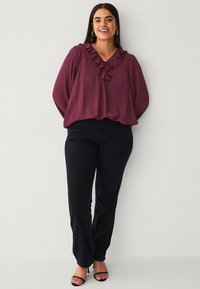 Burgundy bluse med flæser ved halsen og snøre detaljer, parret med mørk denim jeans og sorte hæl sandaler.