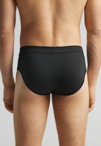 Svarta simbyxor med en slät yta, åtsittande passform och en låg midja. De har enkla sömmar och en klassisk design.