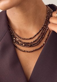 Multi-strand necklace made of round, faceted brown beads, layered in varying lengths, paired with a deep V-neck garment.