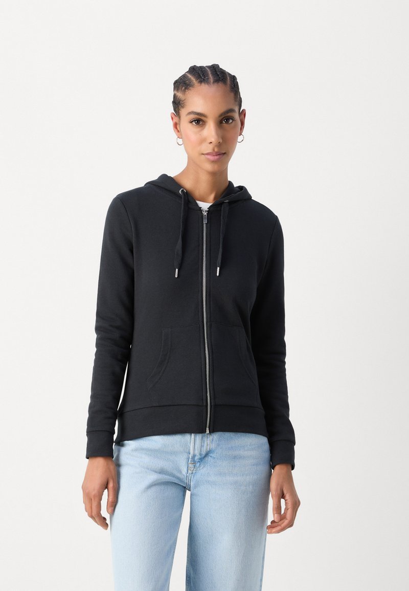 Black zip-up hoodie made of soft fabric, featuring a hood, front pockets, and ribbed cuffs. Worn with light blue jeans.