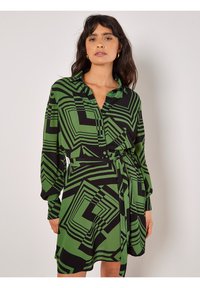 Grünes und schwarzes geometrisches gemustertes Kleid mit langen Ärmeln, Knopfverschluss vorne, Kragen und passendem Gürtel in der Taille. Glatte Stofftextur.