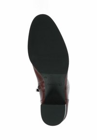Suela de zapato de cuero marrón con suela externa de goma negra texturizada; presenta un acento metálico y branding en la zona del talón.