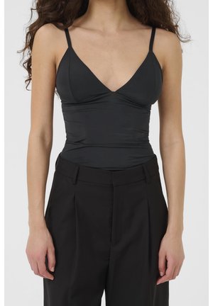 Mujer con un top negro ajustado de tirantes finos metido en unos pantalones negros de talle alto y corte a medida, mostrado desde el cuello hasta las caderas.